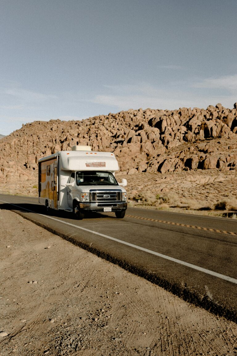 Home RV driving through a scenic desert highway with rocky mountains under a clear sky.